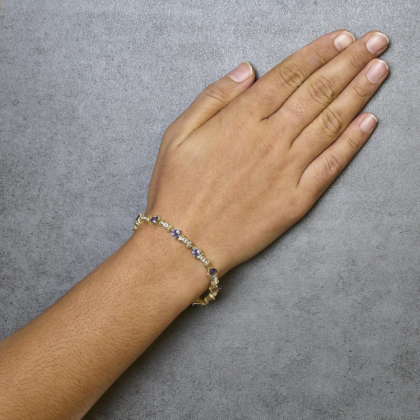 Yellow metal bracelet with alternating blue trillion-shaped gemstones in prong settings and white round gemstones in channel settings, shown worn on a model's wrist with the hand facing down, photographed from above at an angle.