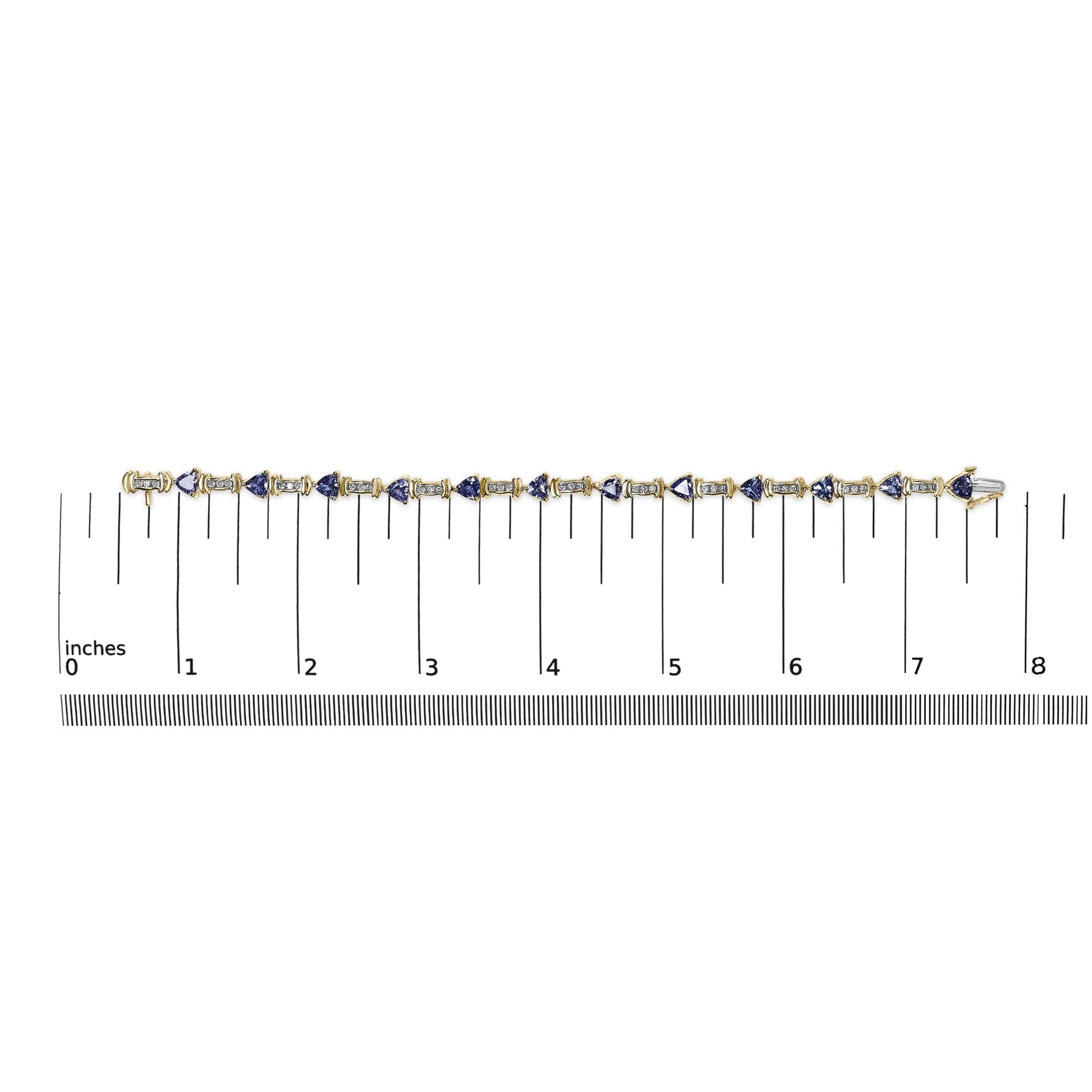 Flat lay image of a yellow metal bracelet with alternating white round gemstones in channel settings and blue trillion-shaped gemstones in prong settings, placed on a ruler for size reference.