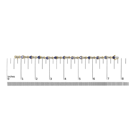 Flat lay image of a yellow metal bracelet with alternating white round gemstones in channel settings and blue trillion-shaped gemstones in prong settings, placed on a ruler for size reference.