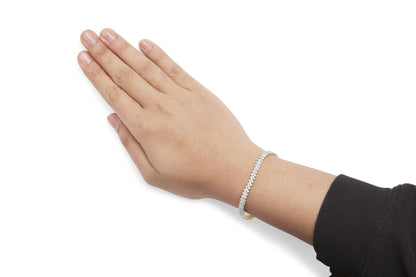 Yellow metal bracelet with prong-set round white gemstones, shown on a model's wrist from a top-down angle.