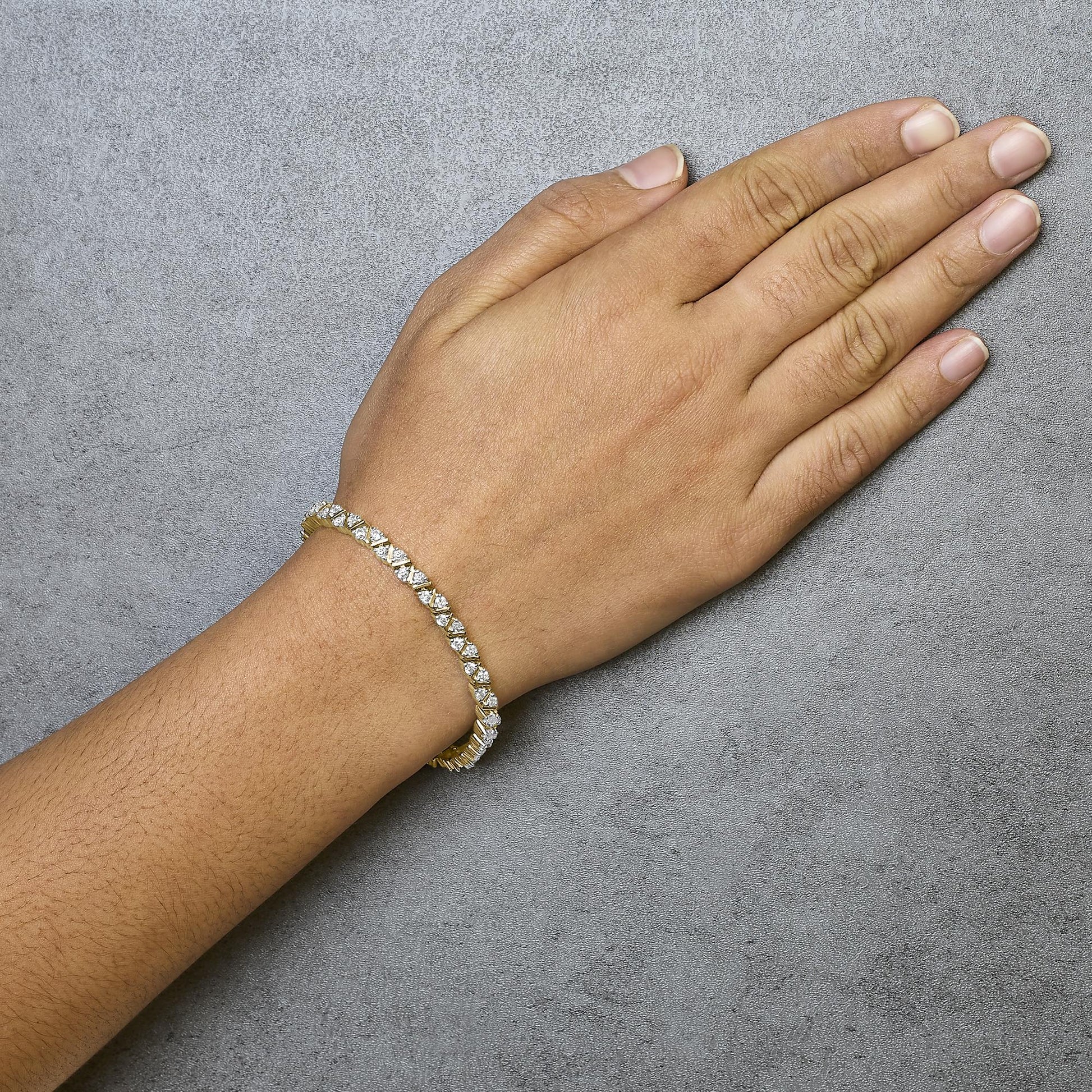 Yellow metal bracelet with round white gemstones in 3-prong settings, worn on a model’s wrist, top-down angle.