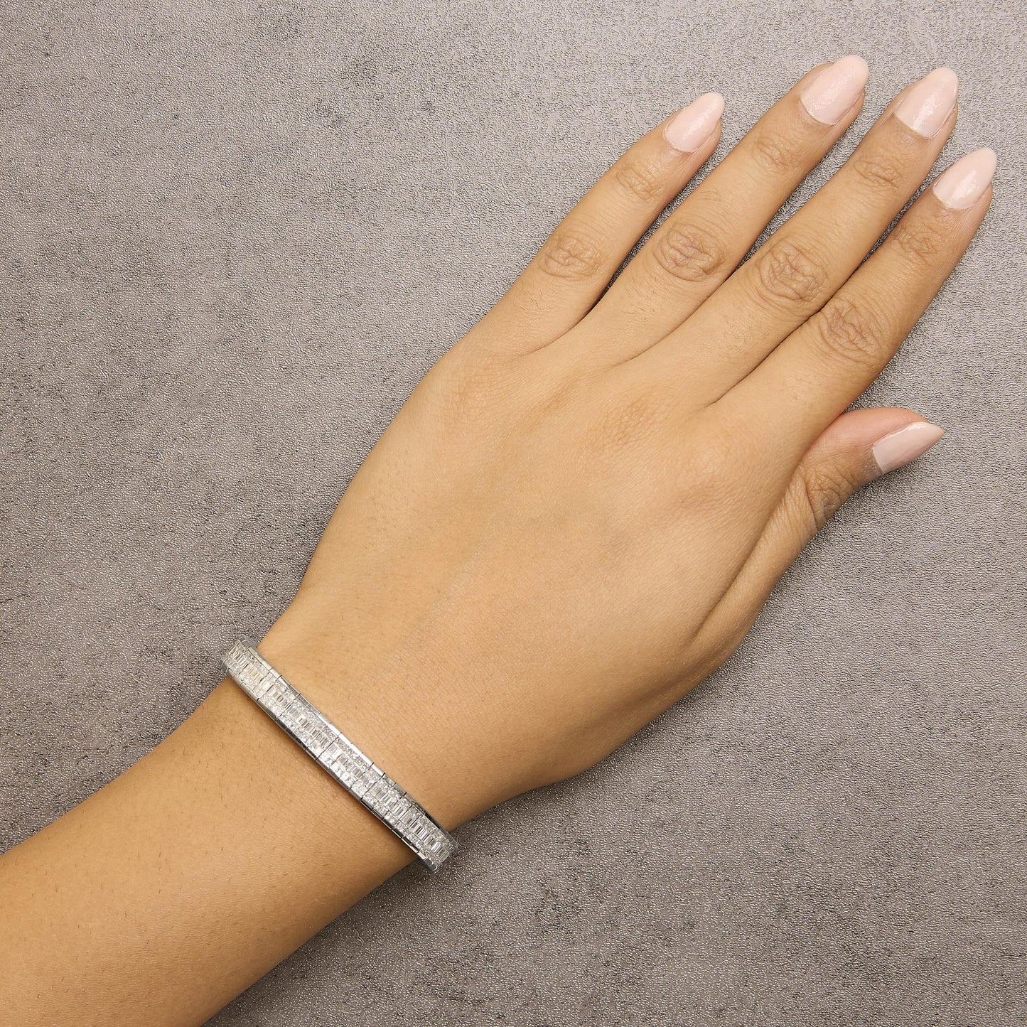 White metal bracelet with white baguette and princess shape gemstones in channel and invisible settings, shown worn on wrist in a top-down angle.