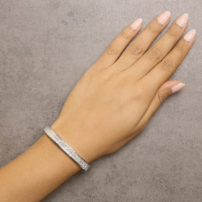 White metal bracelet with white baguette and princess shape gemstones in channel and invisible settings, shown worn on wrist in a top-down angle.
