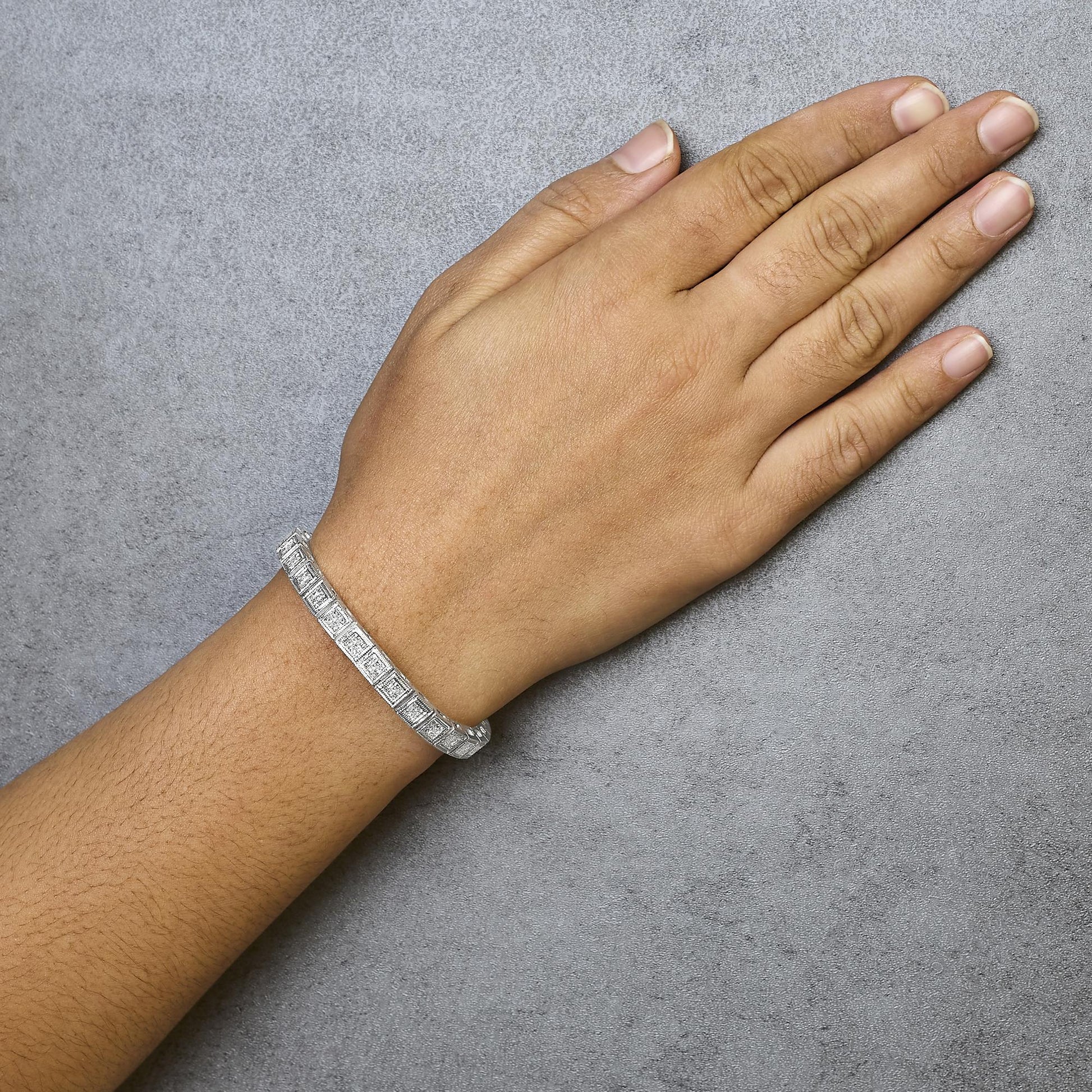 White metal bracelet with princess-shaped white gemstones in an invisible setting, shown worn on model's wrist from a top-down angle.