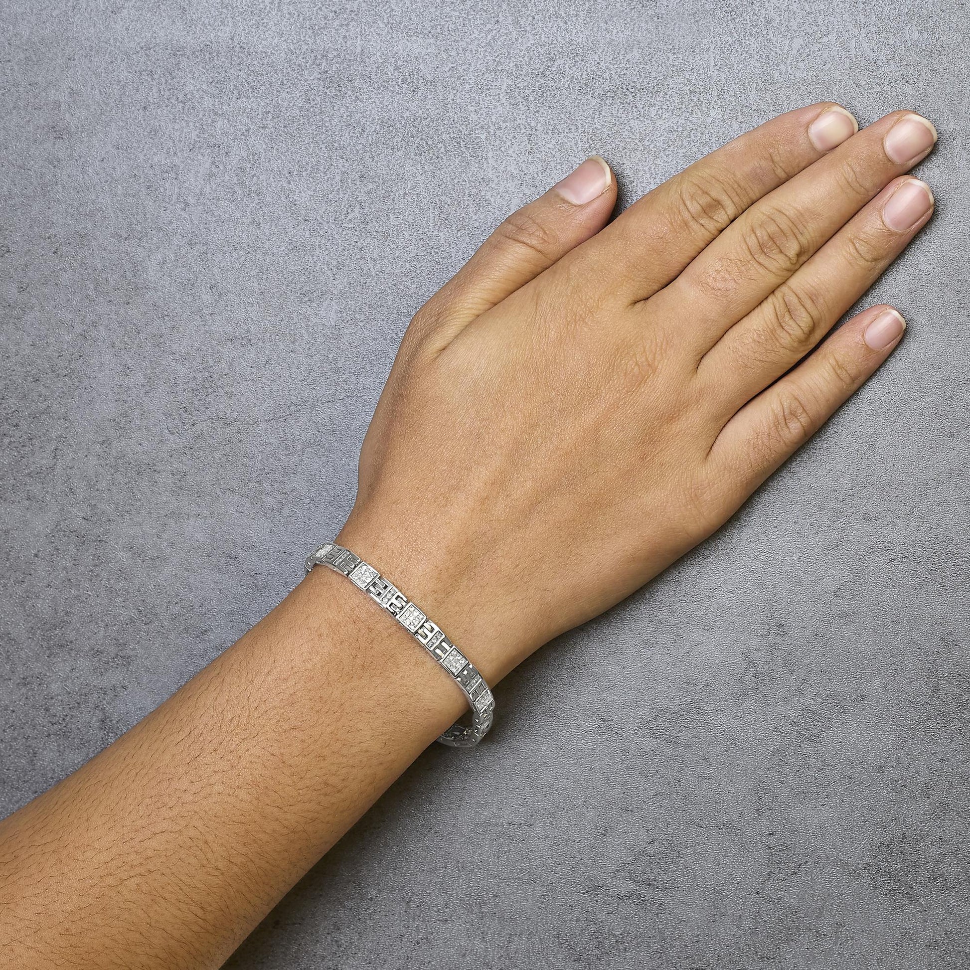 White metal bracelet with white and blue princess-shaped gemstones, worn on a model's wrist, shown from above.