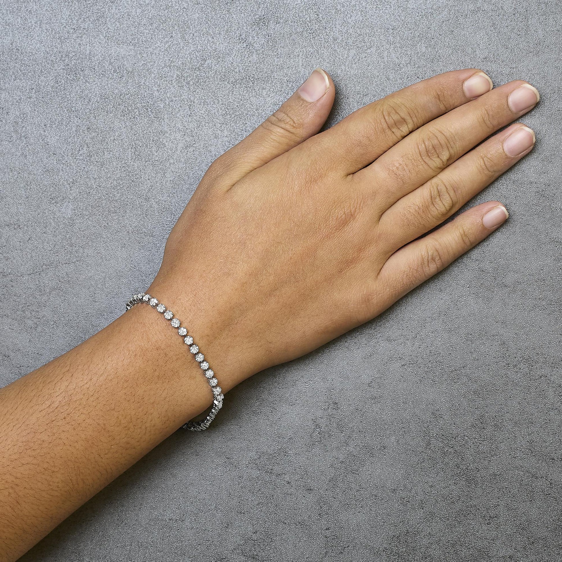 White metal bracelet with round white gemstones in prong settings, shown on a model's wrist from a top-down angle.