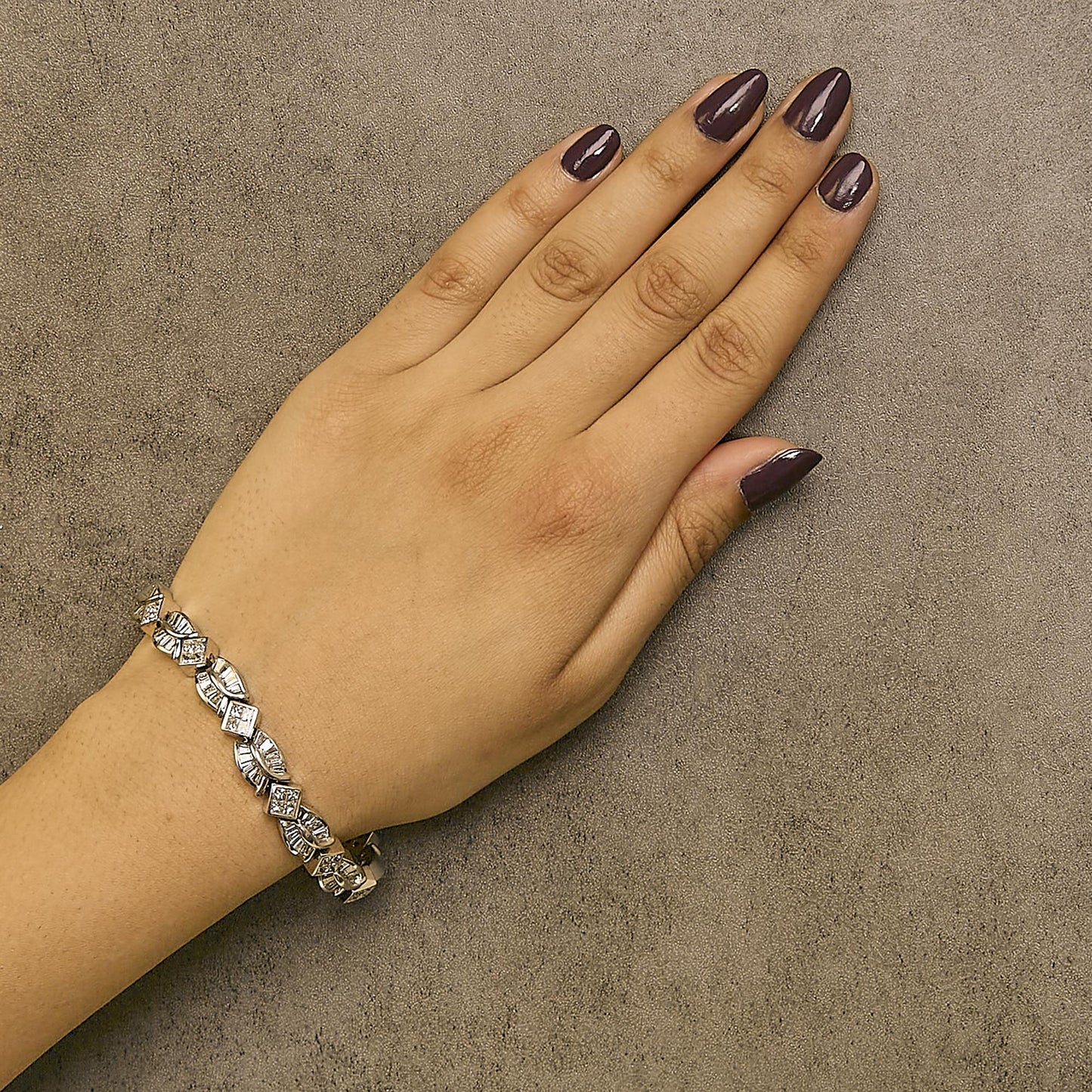 White bracelet with baguette and princess shape white gemstones in channel and invisible settings, shown worn on a model's wrist from a top-down angle.