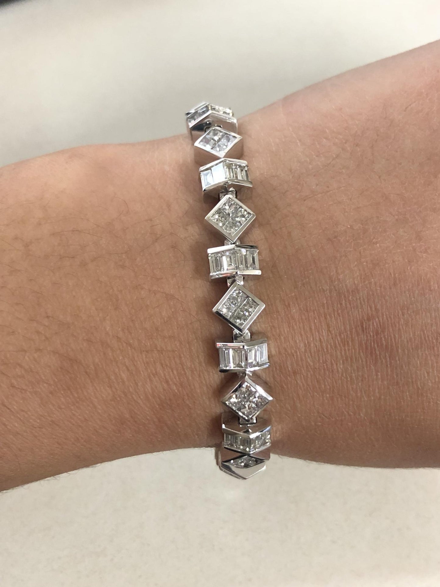 White metal bracelet featuring alternating baguette and princess shape white gemstones, shown worn on a model’s wrist, photographed from a top angle.