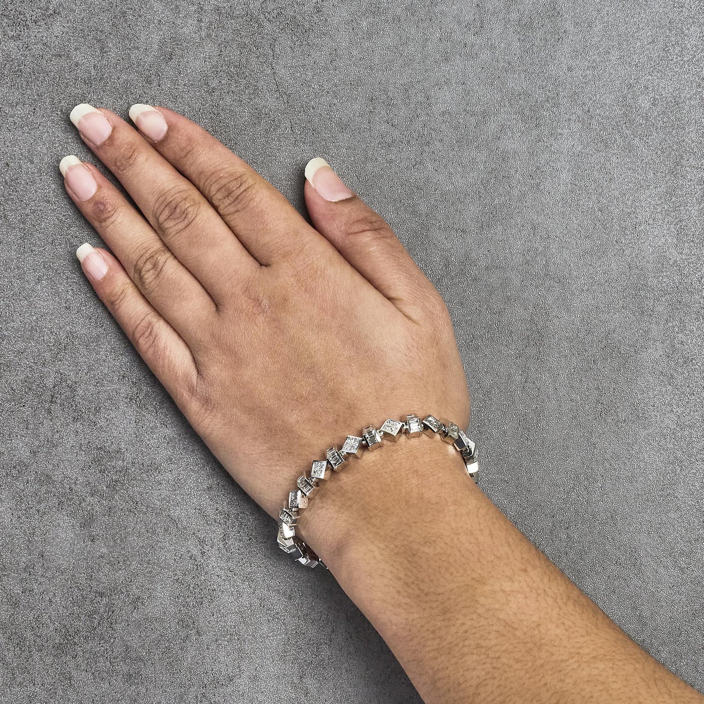 White metal bracelet with alternating baguette shaped and princess shaped white gemstones, shown worn on a model's wrist, top-down angle.