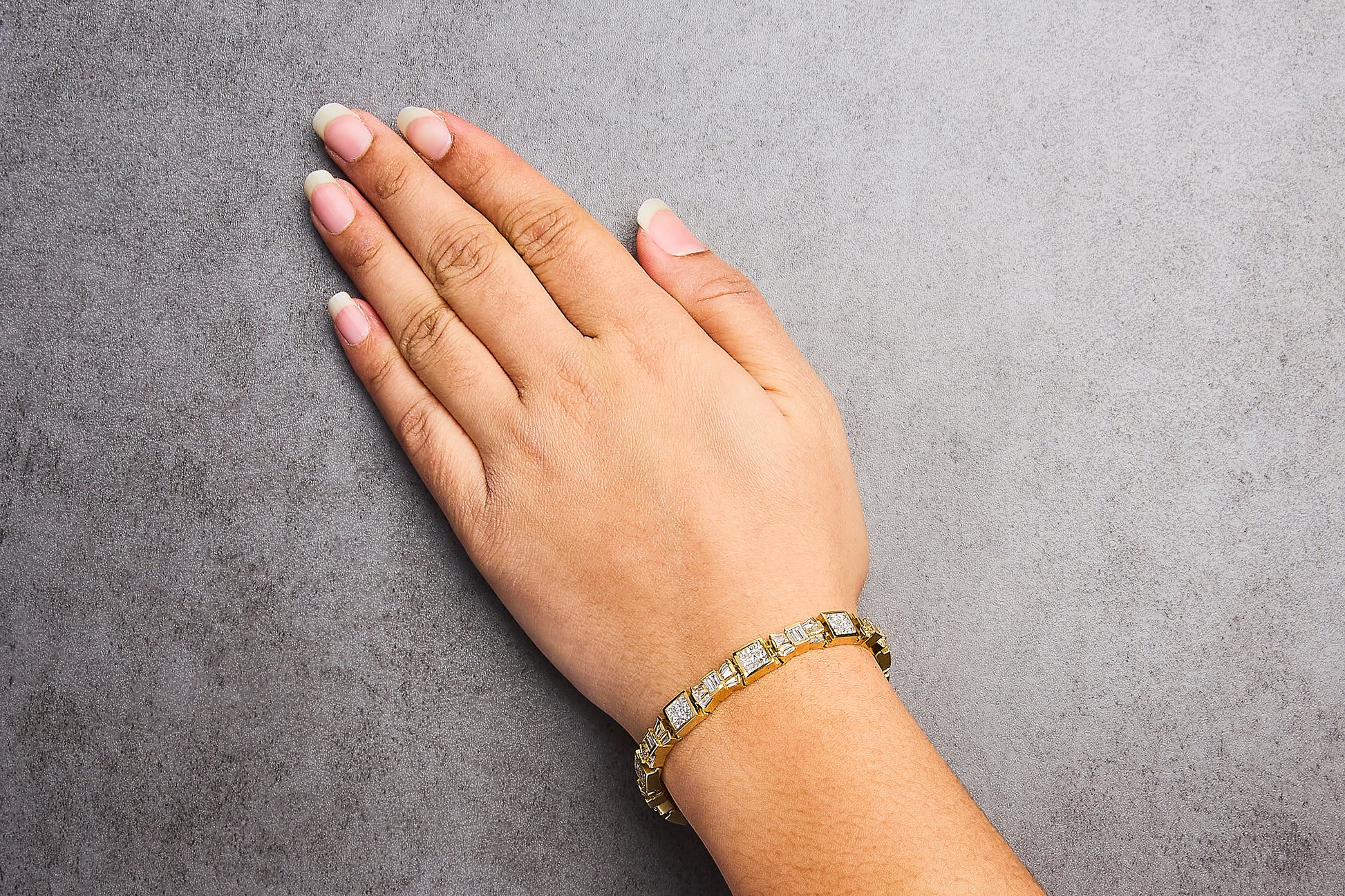Yellow metal bracelet with white baguette and princess shape gemstones, shown worn on a model's wrist from a top angle.