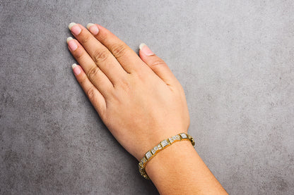 Yellow metal bracelet with white baguette and princess shape gemstones, shown worn on a model's wrist from a top angle.