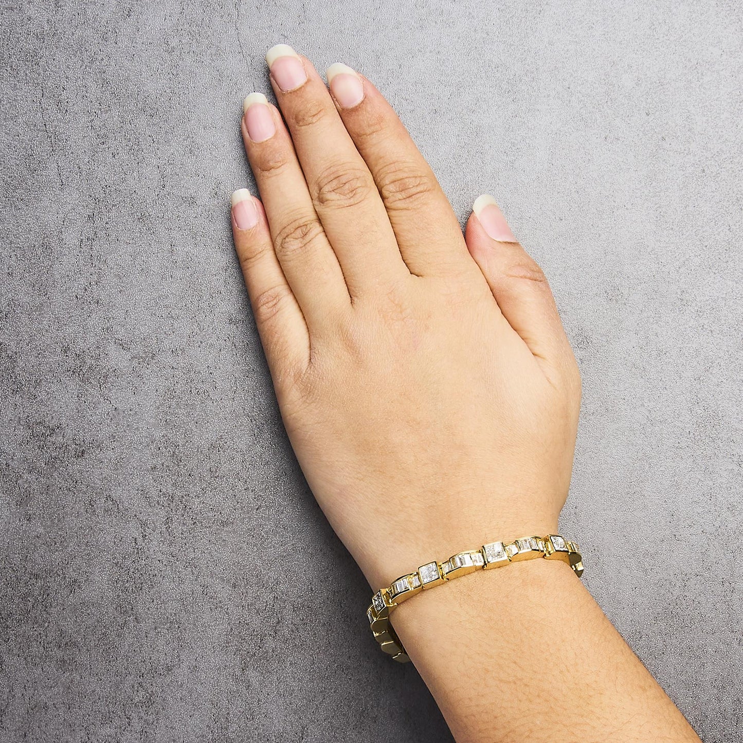 Bracelet with alternating channel-set baguette and invisible-set princess white gemstones in yellow metal, shown worn on a model's wrist from an overhead angle.