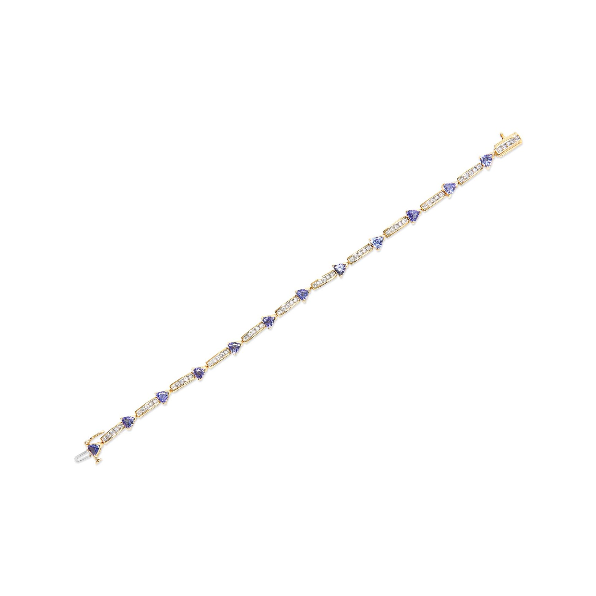 Yellow metal bracelet with alternating rectangular segments of channel-set white round gemstones and prong-set blue trillion gemstones, shown in a diagonal top-down view.
