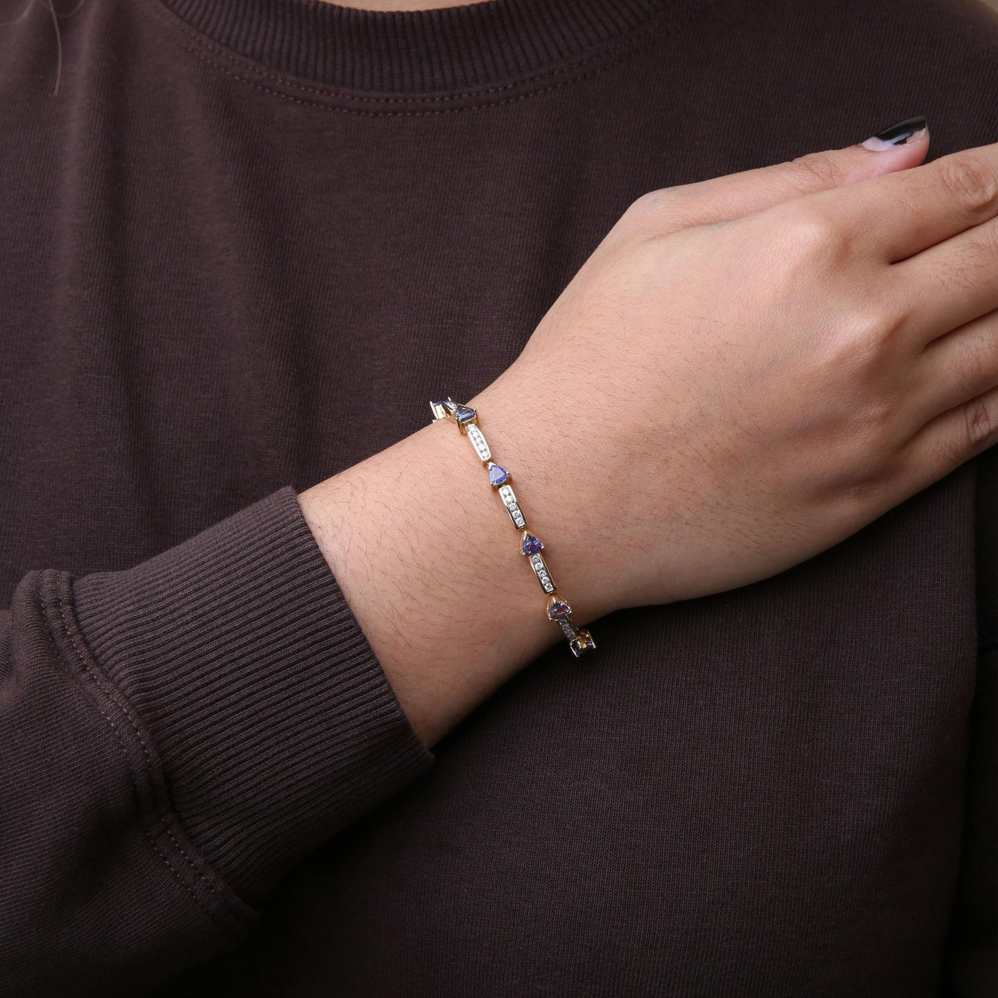 Yellow bracelet with round white gemstones in channel settings and blue trillion-shaped gemstones in prong settings, shown on wrist at an angled side view.