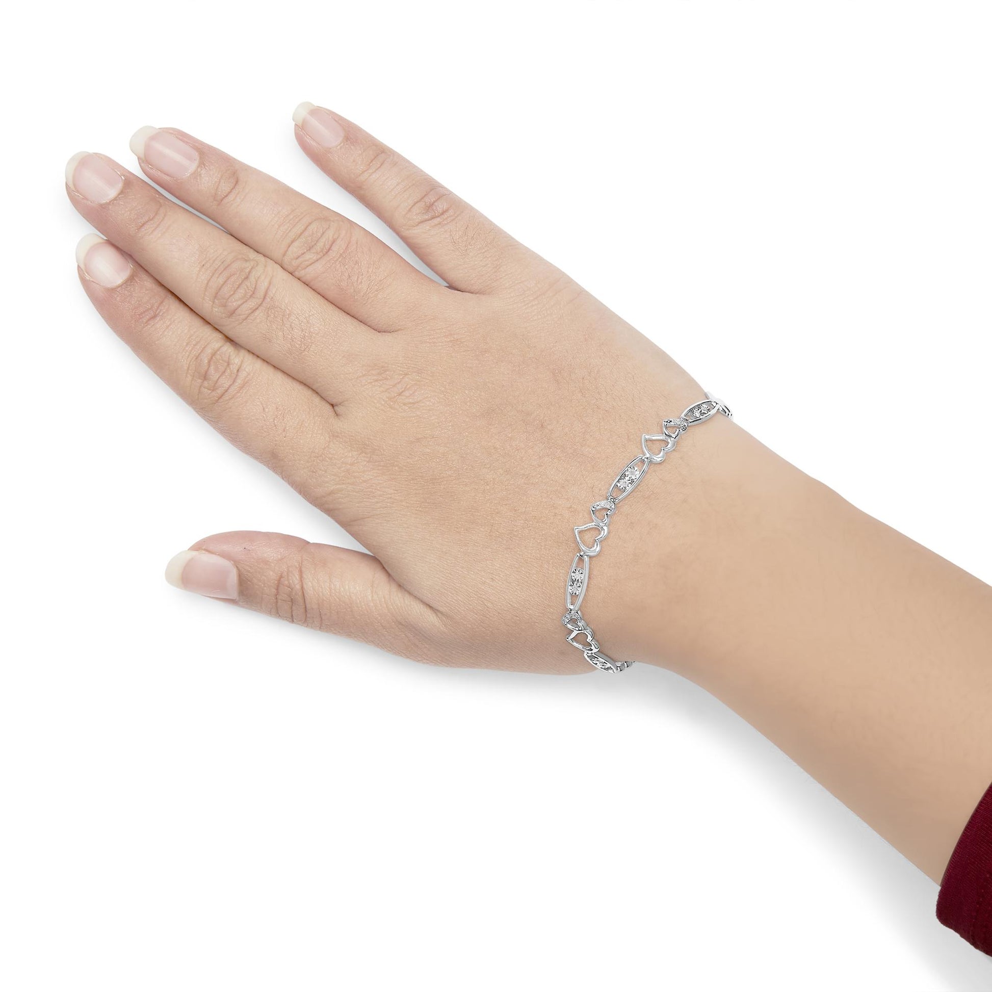 White metal bracelet with alternating heart shapes and oval links set with round white gemstones, shown on top of a model's wrist with hand angled downward.