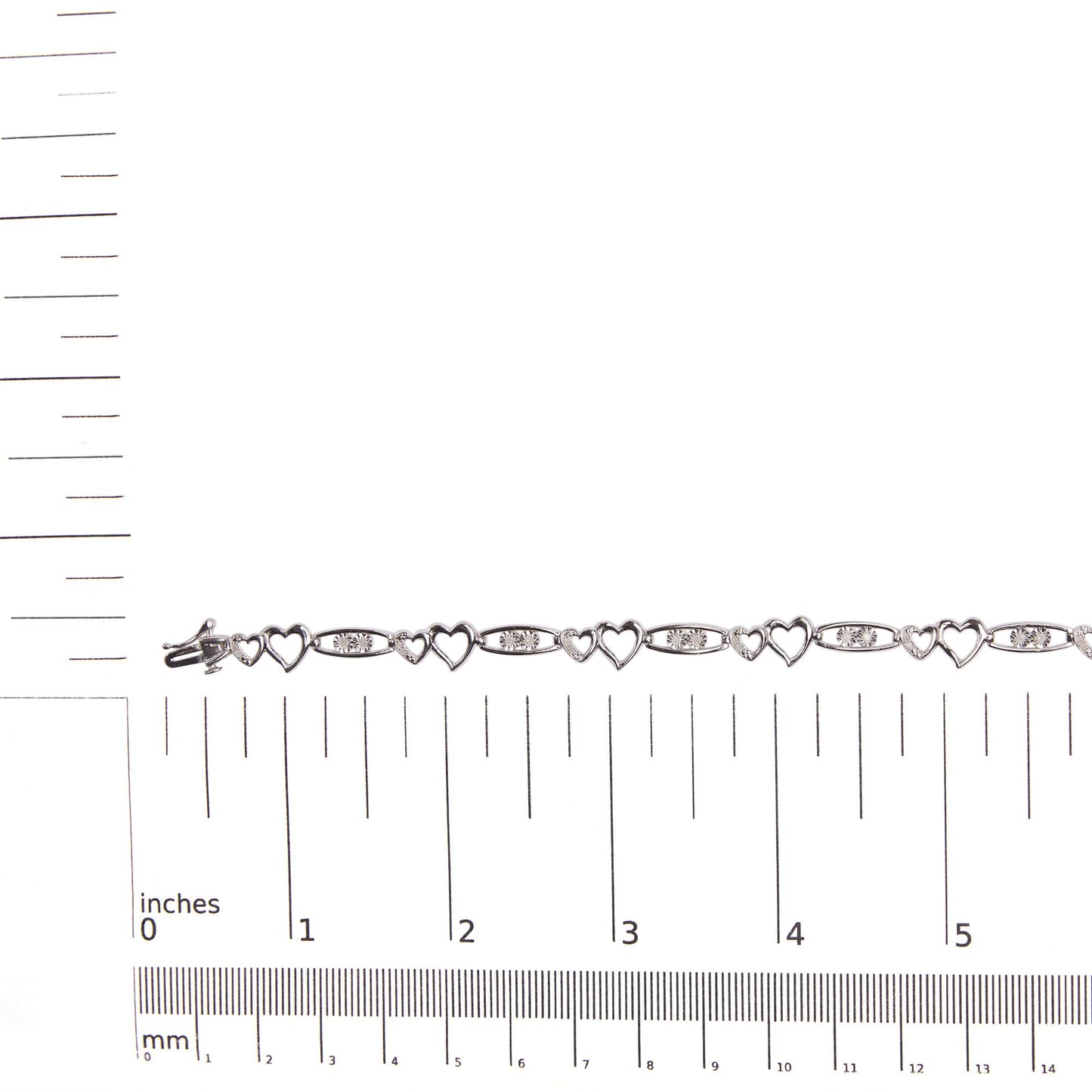 White metal bracelet with alternating open heart shapes and oval links set with round white gemstones, shown flat on a ruler for size reference, top-down view.