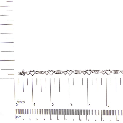 White metal bracelet with alternating open heart shapes and oval links set with round white gemstones, shown flat on a ruler for size reference, top-down view.