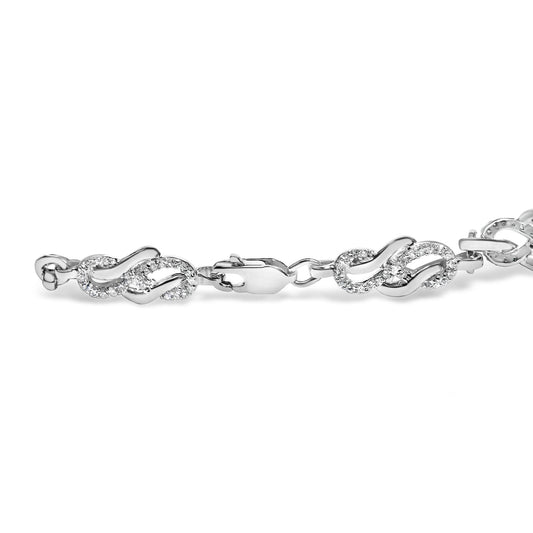 Close-up side angle of a white metal bracelet with linked sections featuring a flowing, intertwined design accented with round white gemstones in a pave setting.