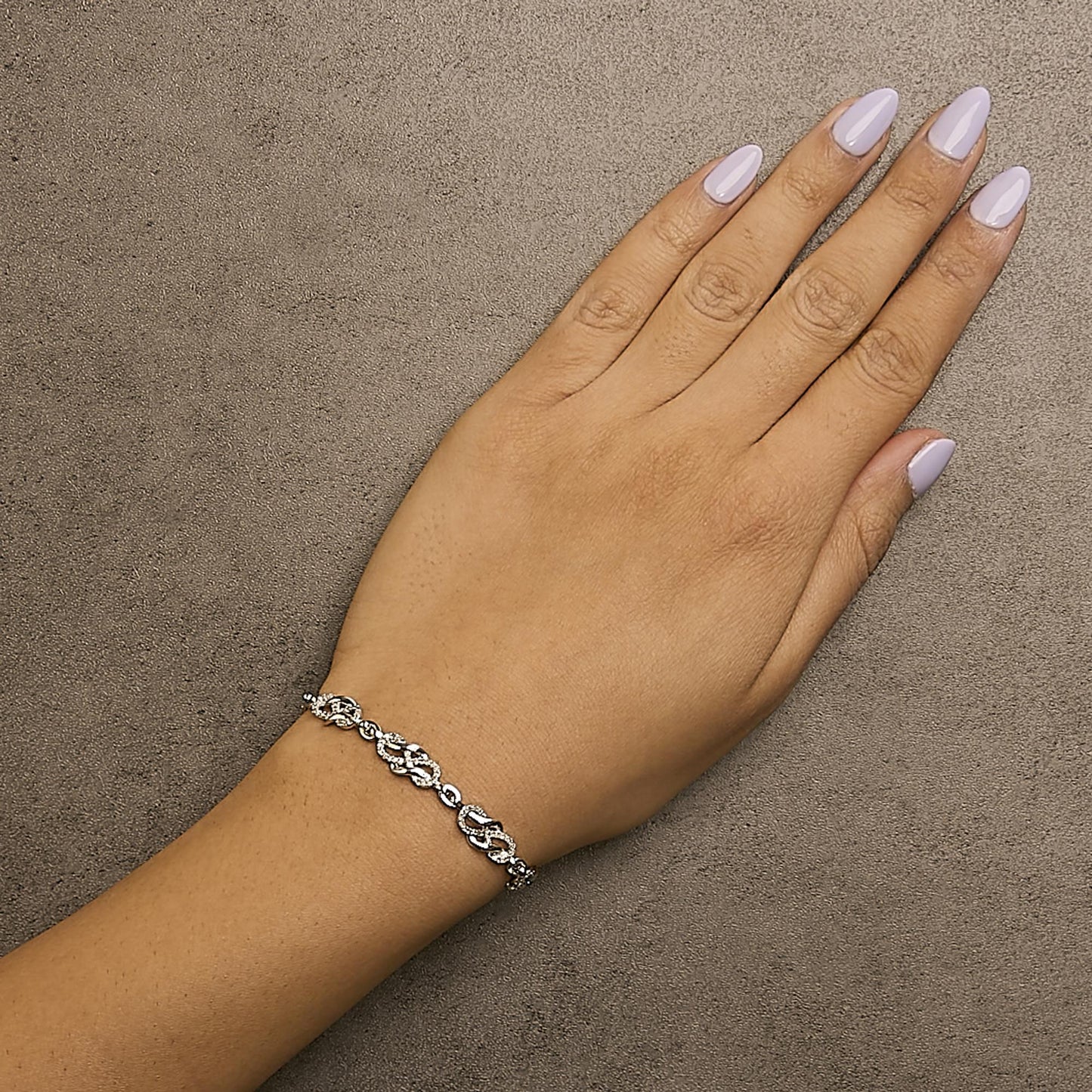 White metal bracelet with interlocking links set with round white gemstones in a pave setting, worn on a model's wrist, shot from above.