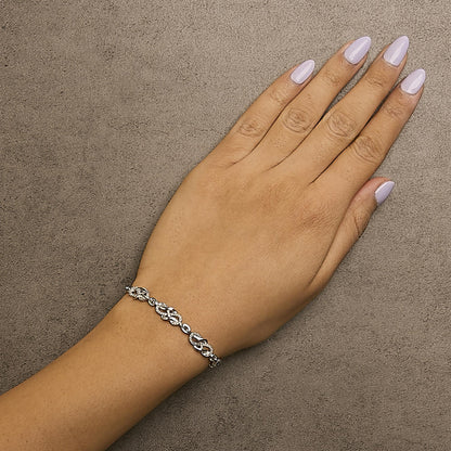 White metal bracelet with interlocking links set with round white gemstones in a pave setting, worn on a model's wrist, shot from above.