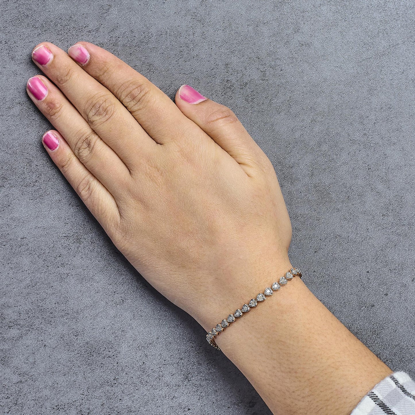 Rose metal bracelet with white round gemstones in miracle setting, shown on the wrist of a model from a top-down angle.