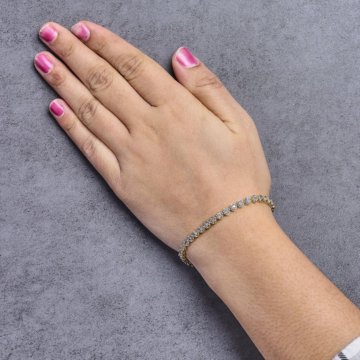 Yellow metal bracelet with round white gemstones in miracle setting, shown on model's wrist angled from above.