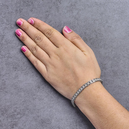 White metal bracelet with round white gemstones in prong settings, shown on a model's wrist from a top angle.