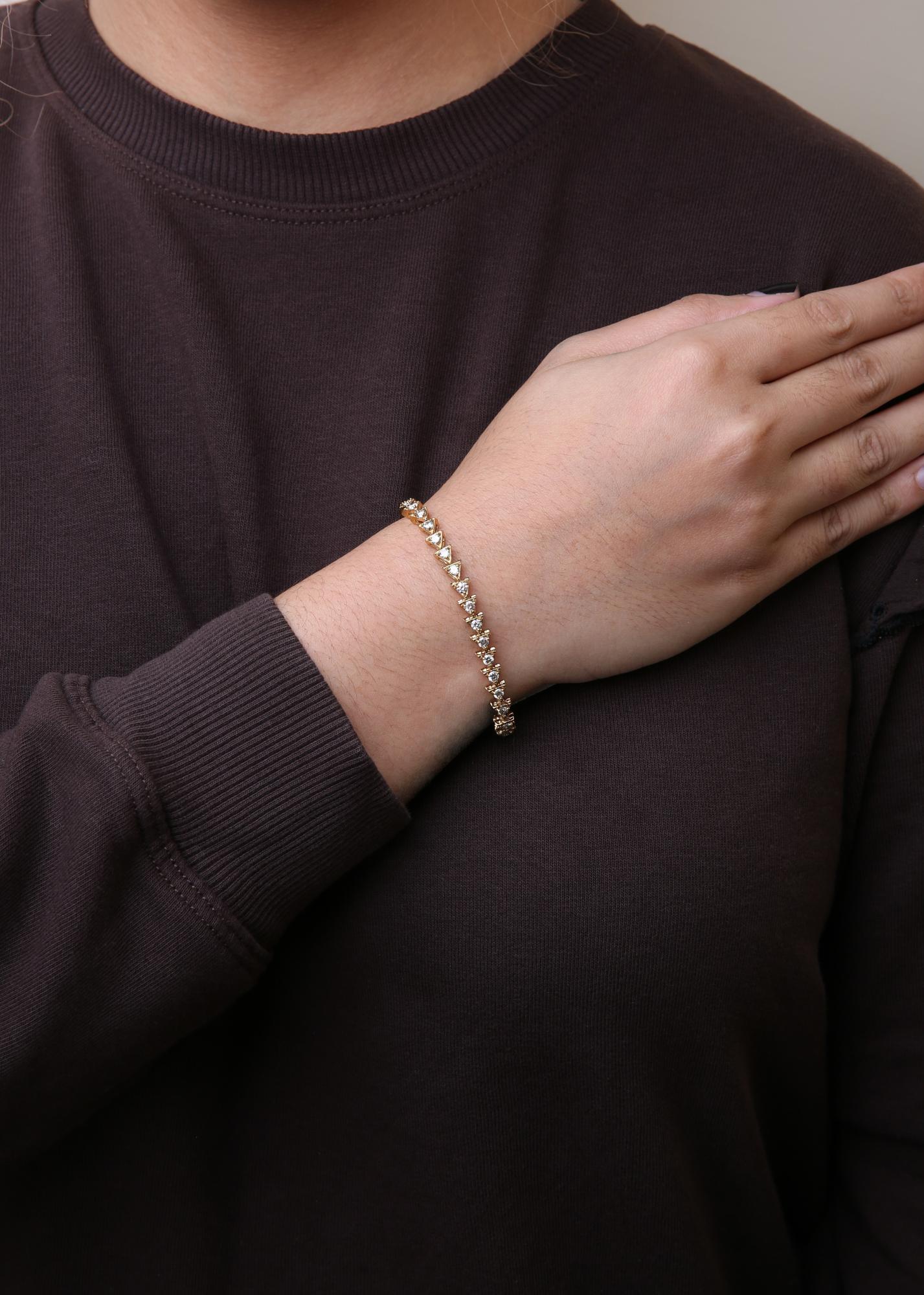 Yellow metal bracelet with white round gemstones in prong settings, shown on a model's wrist from a front angle.