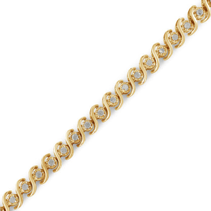 Diagonal close-up of a yellow metal bracelet featuring round white gemstones set in a repeating swirling design.