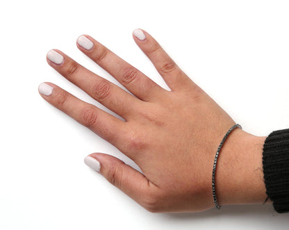 White metal bracelet with round black gemstones in prong settings, worn on a model's wrist, shown from a top-side angle.