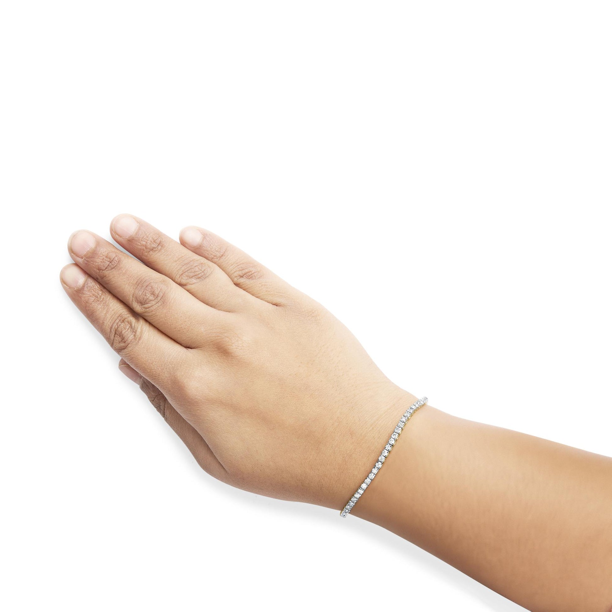 Close-up photo of a yellow metal bracelet with round brownish gemstones in 4-prong settings, worn on a model's wrist, shot from above.