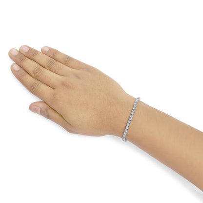 White metal bracelet with round white gemstones in 4-prong settings, shown on a model's wrist with hand flat, photographed from above at an angle.