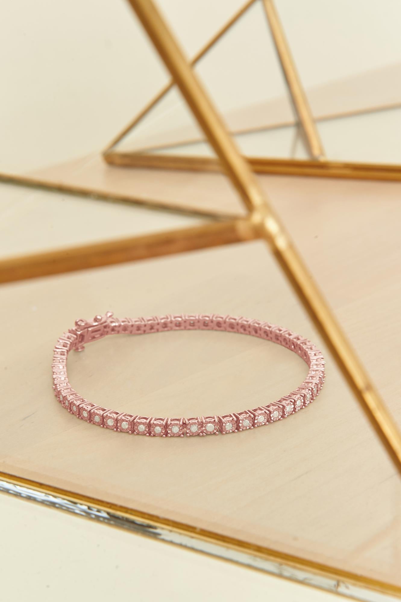 Rose metal bracelet with round white gemstones in a miracle setting, shown in a flat lay angled view on a reflective surface with gold geometric framing.