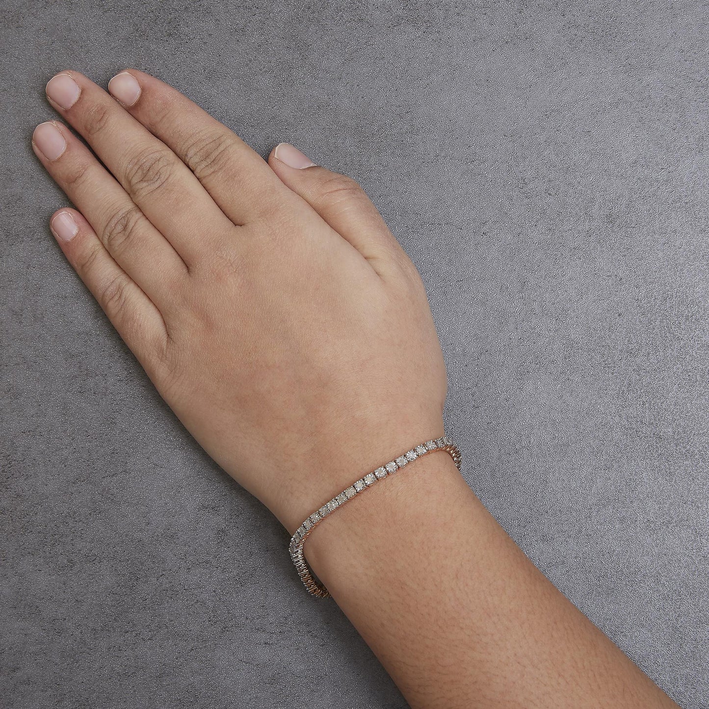 Rose metal bracelet with round white gemstones in miracle setting, shown from above on a model's wrist.