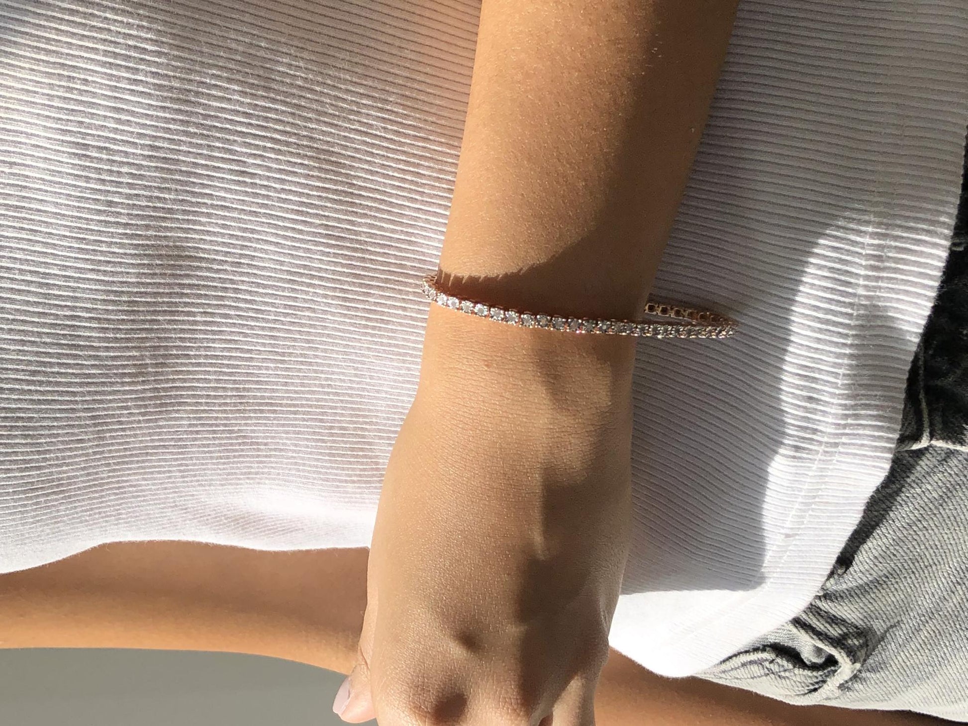 Close-up front angle of a rose-colored bracelet with round white gemstones in a miracle setting, shown worn on a model's wrist.