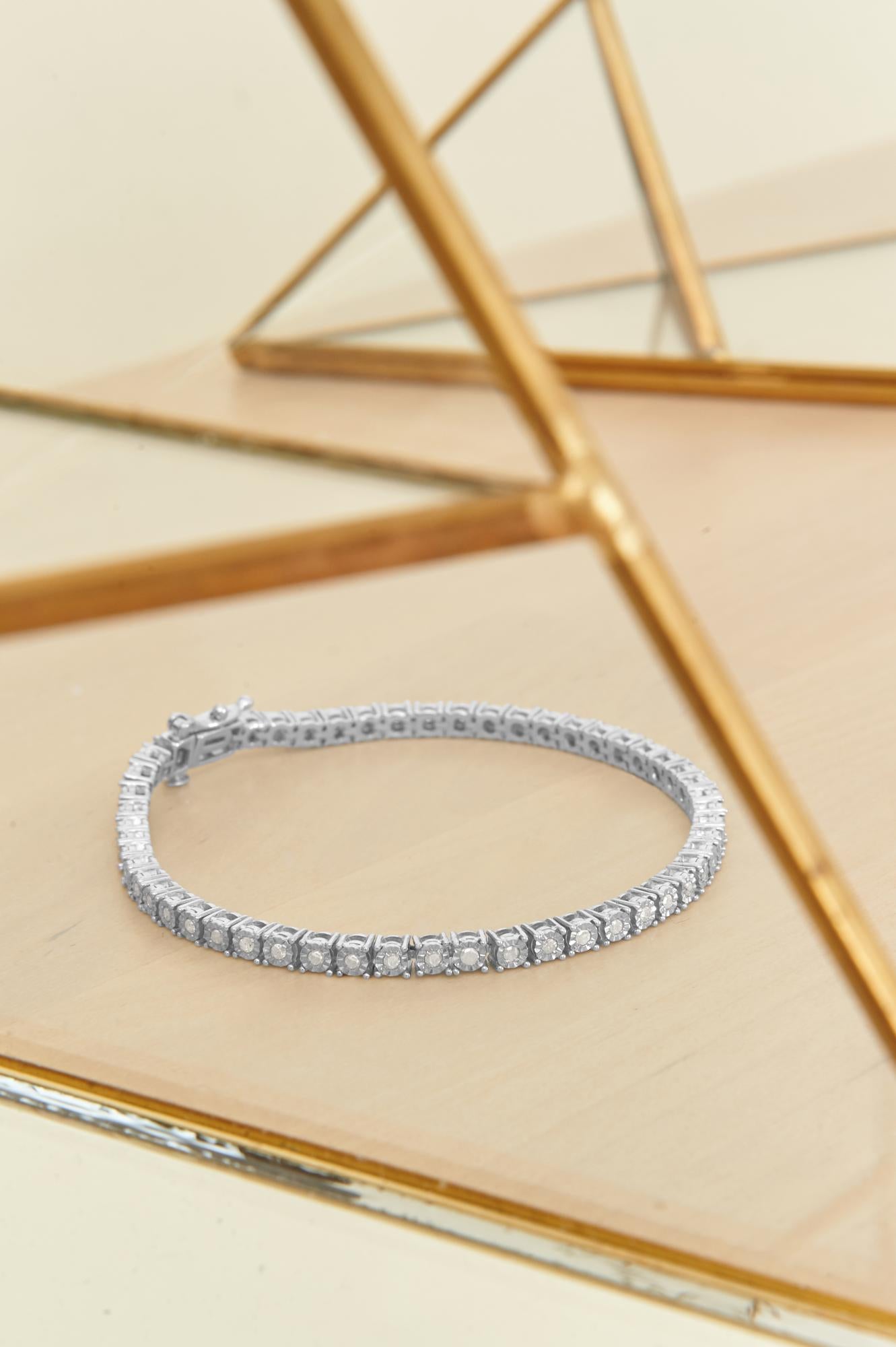White bracelet with round white gemstones in miracle setting, shown laid flat on a reflective surface, photographed from a high front angle.