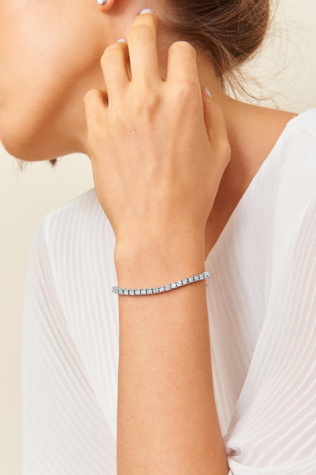 White metal bracelet with round white gemstones in miracle setting, shown on a model's wrist in a side profile angle.