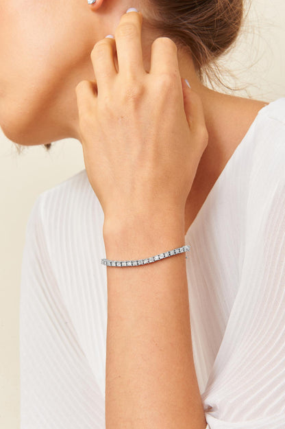 White metal bracelet with round white gemstones in miracle setting, shown on a model's wrist in a side profile angle.