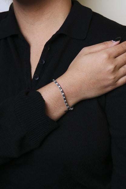 White metal bracelet with alternating blue and white round and rose-shaped gemstones in miracle setting, worn on model's wrist, angled front view.