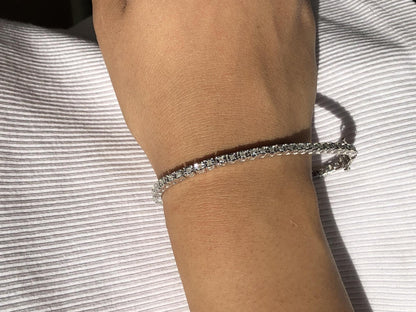 Close-up front angle of a white metal bracelet with round white gemstones in a miracle setting, worn on a model's wrist.