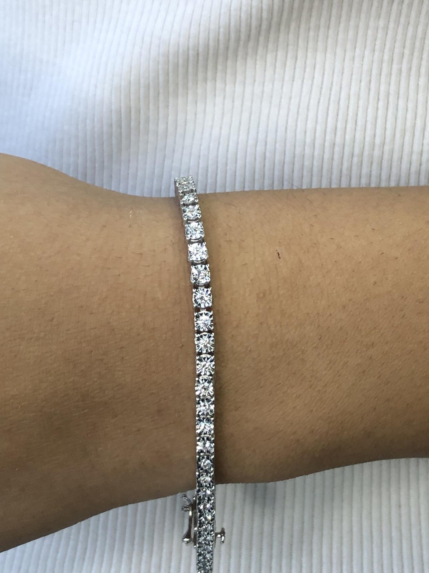 White metal bracelet with round white gemstones in a miracle setting, shown on a model’s wrist from a side angle.