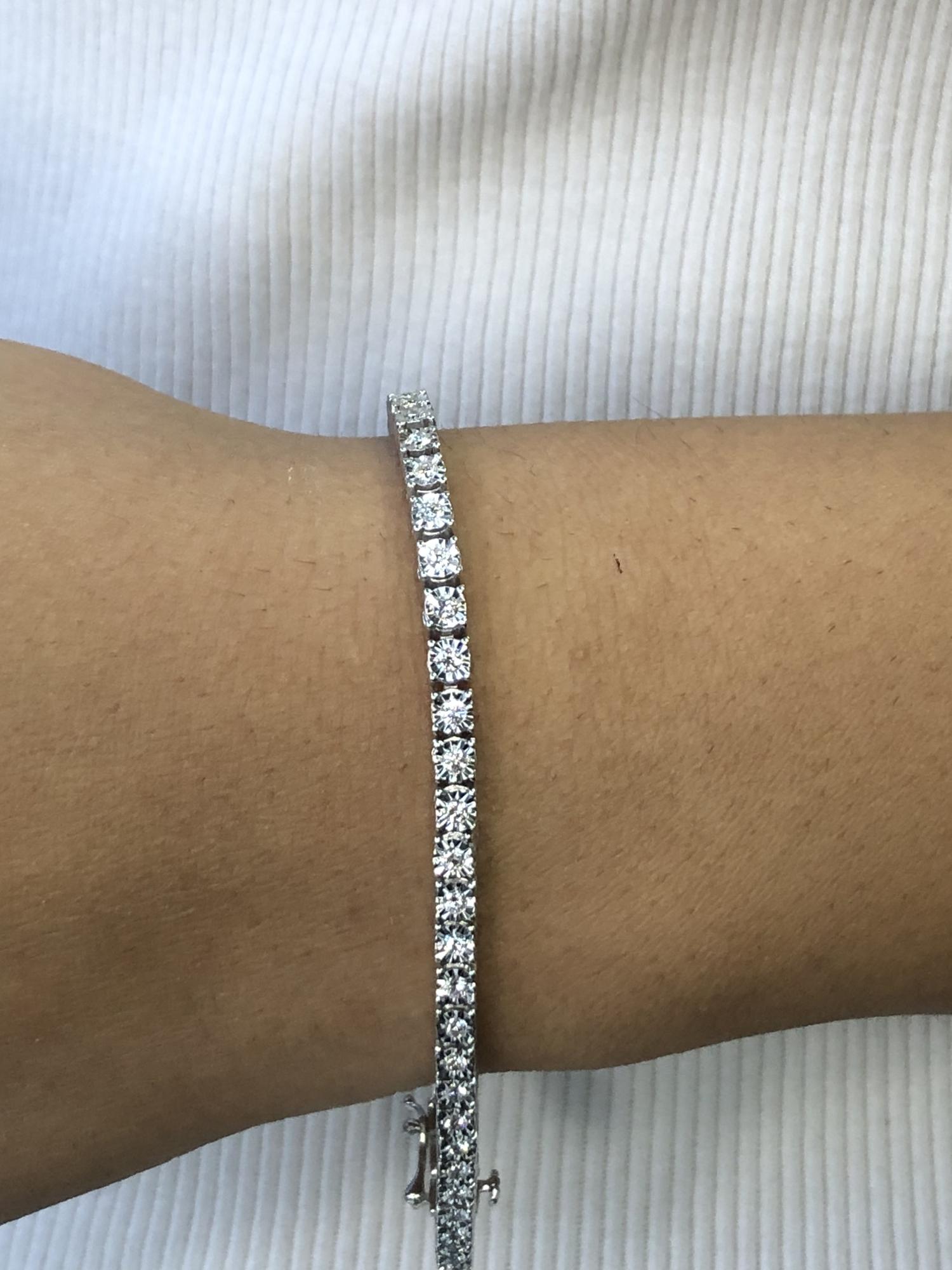 White metal bracelet with round white gemstones in a miracle setting, shown on a model’s wrist from a side angle.