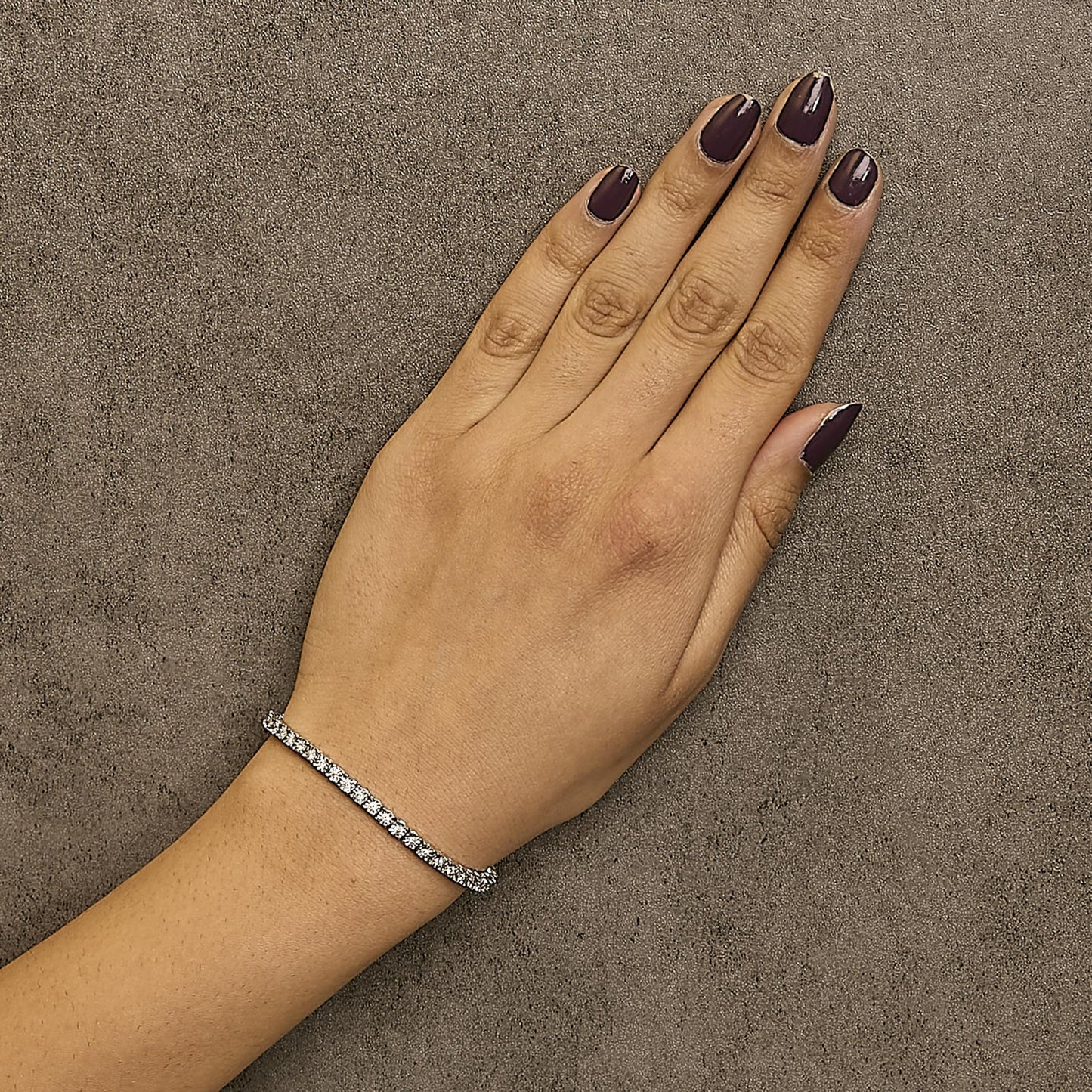 White metal bracelet with round white gemstones in miracle setting, worn on a model's wrist, top-down angle.