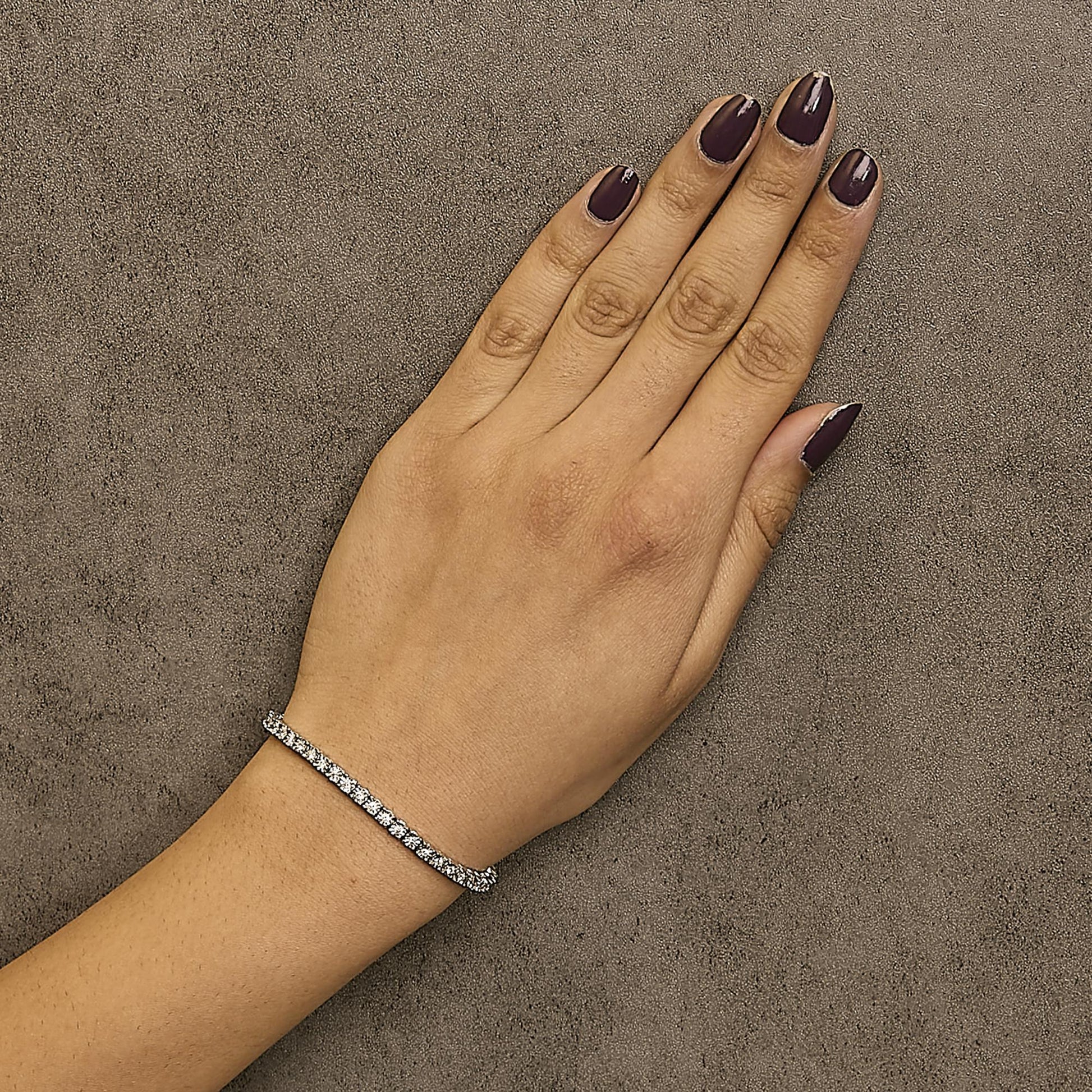 White metal bracelet with round white gemstones in miracle setting, worn on a model's wrist, top-down angle.