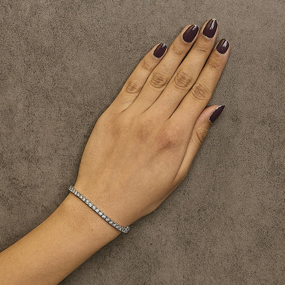 White metal bracelet with round white gemstones in miracle setting, worn on a model's wrist, top-down angle.