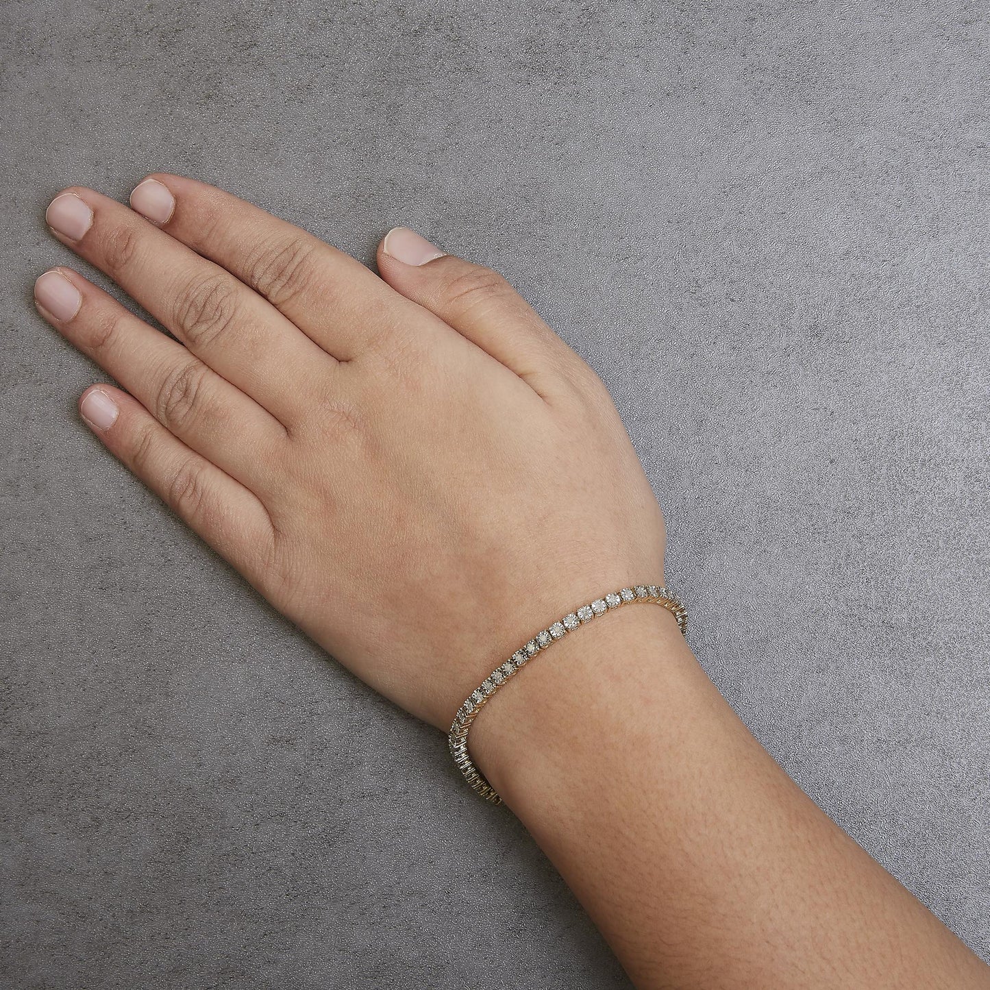 Yellow metal bracelet with round white gemstones in miracle setting, shown on a model's wrist, angled from above.
