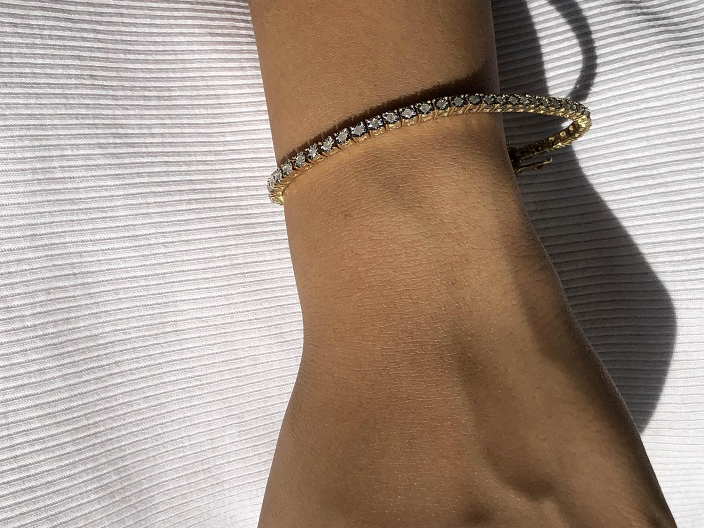 Close-up side angle of a yellow bracelet with round white gemstones in a miracle setting, shown worn on a model's wrist.