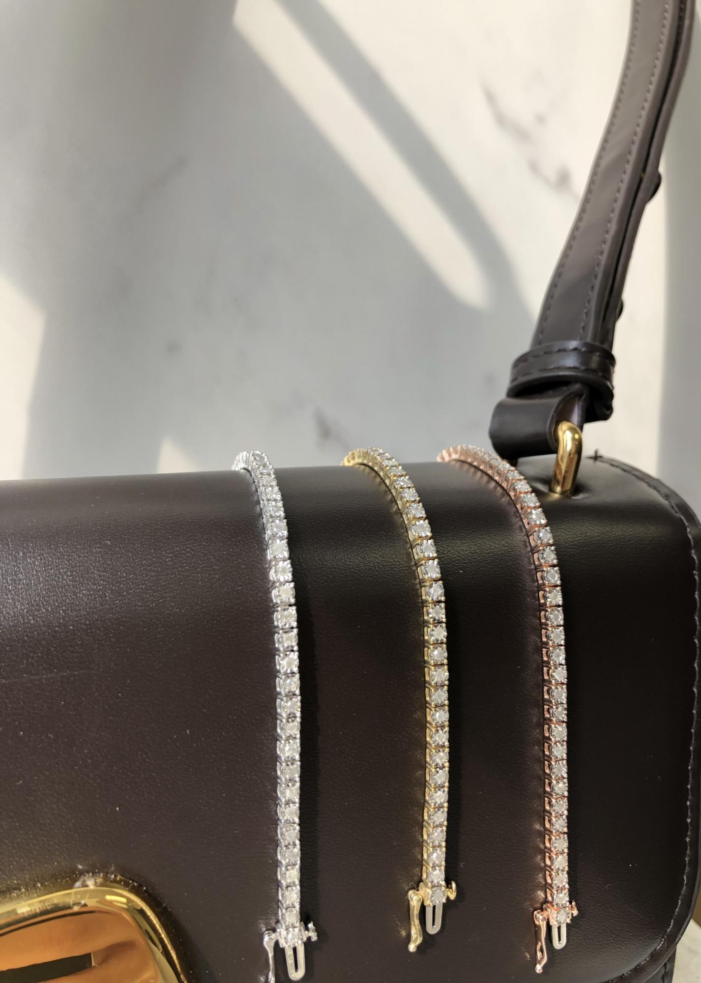 Close-up front angle shot of a yellow metal bracelet with round white gemstones in a miracle setting, displayed on a black bag strap.