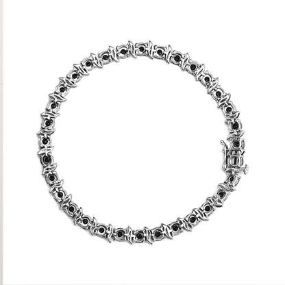 Top-down view of a white metal bracelet with round black gemstones in miracle settings encircling the entire piece.