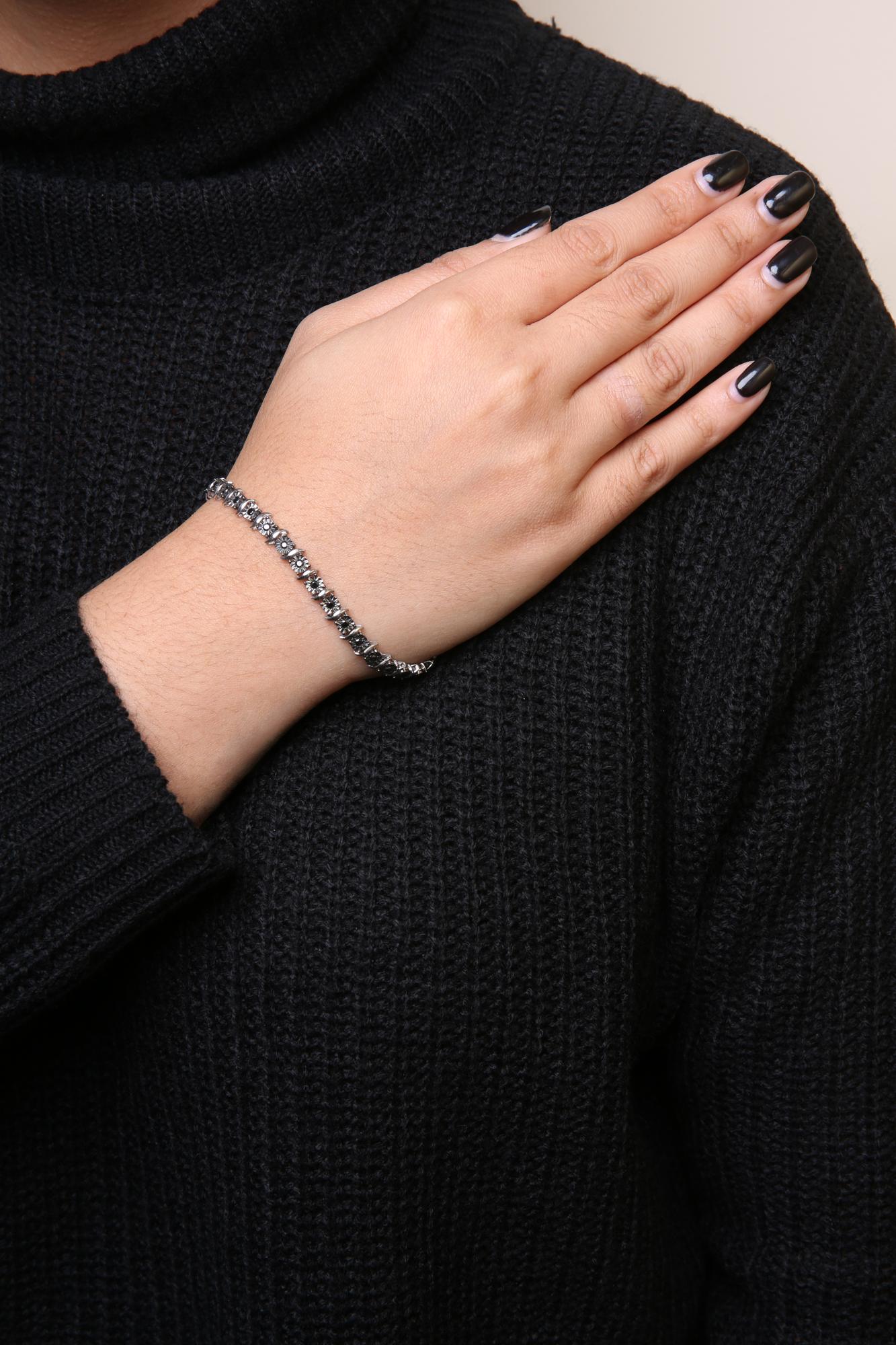 White metal bracelet with round black gemstones in miracle setting, worn on a model's wrist, angled view.